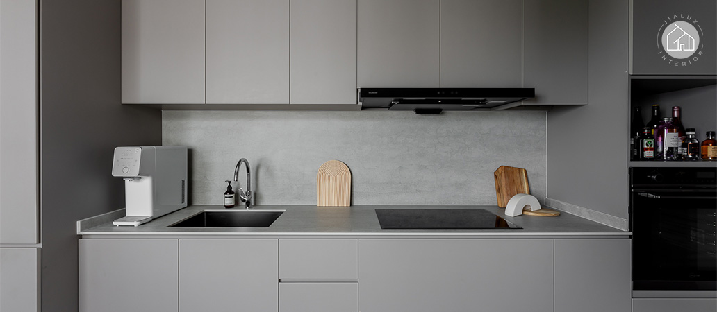 A contemporary kitchen area with sleek grey cabinetry, a built-in black stovetop, and a white water dispenser on a grey countertop.