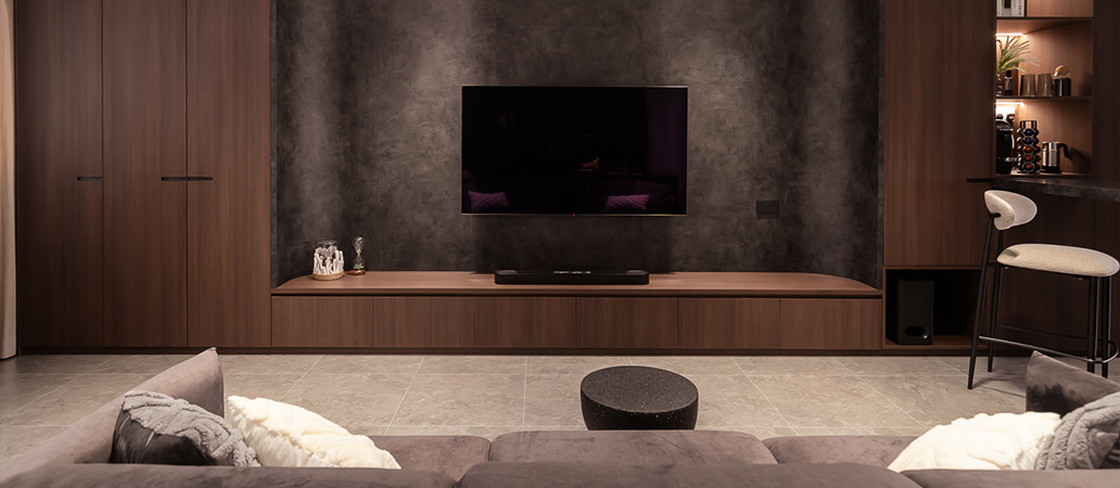 Modern living room with wall-mounted TV, wooden cabinet, gray sectional sofa, and small bar area.