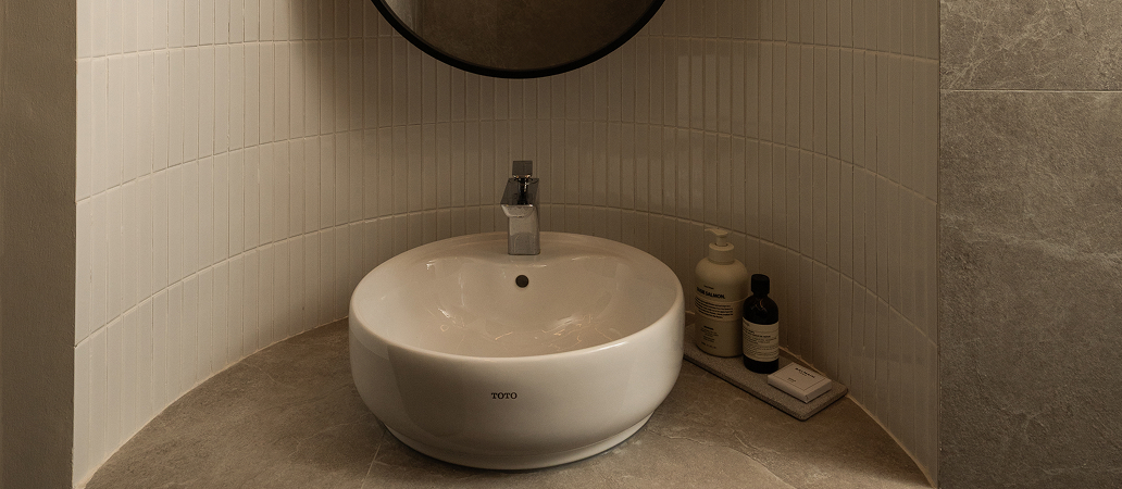 Curved tiled bathroom niche with oval mirror and lighting.